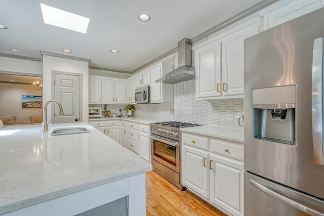 kitchen featuring light wood-type flooring, stainless steel appliances, sink, wall chimney range hood, and white cabinetry