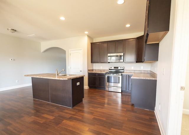 kitchen with a center island with sink, sink, dark hardwood / wood-style floors, light stone countertops, and stainless steel appliances