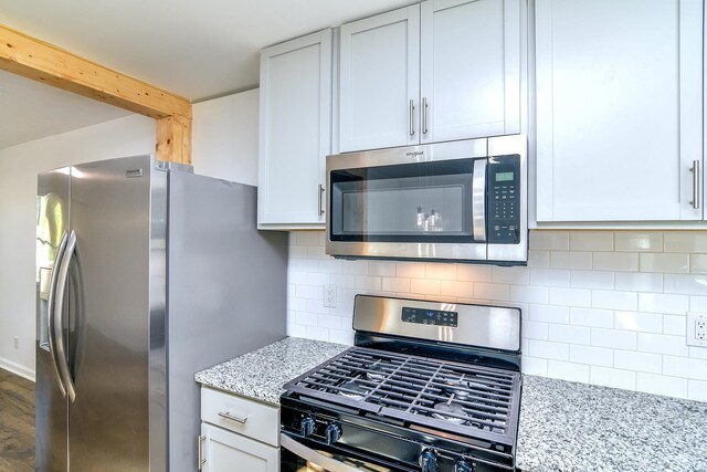 kitchen with dark wood-type flooring, decorative backsplash, appliances with stainless steel finishes, light stone counters, and white cabinetry