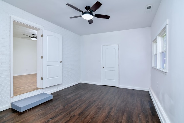 unfurnished bedroom featuring dark hardwood / wood-style floors, ceiling fan, and brick wall