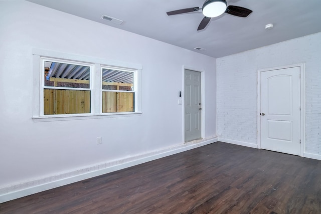 spare room featuring dark hardwood / wood-style flooring, ceiling fan, and brick wall