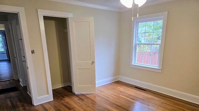 unfurnished bedroom featuring dark hardwood / wood-style flooring, crown molding, and a closet