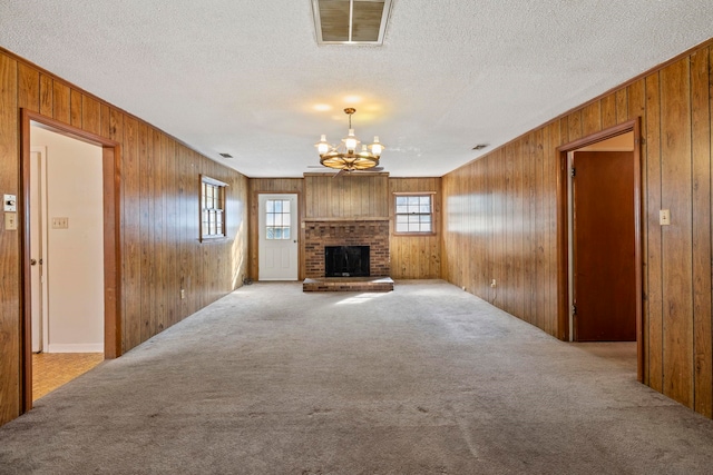 unfurnished living room with light colored carpet, a fireplace, a textured ceiling, and a notable chandelier