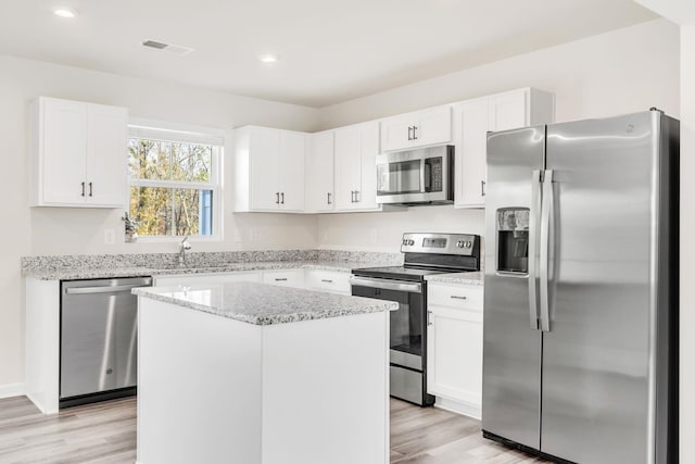 kitchen with light stone countertops, light hardwood / wood-style floors, appliances with stainless steel finishes, a kitchen island, and white cabinetry