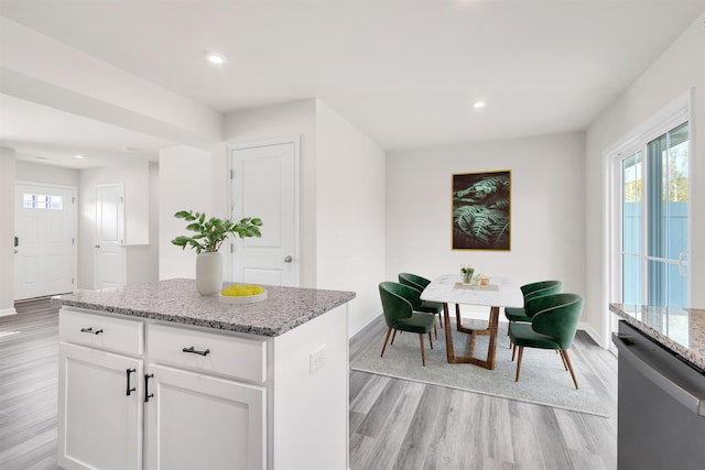 kitchen with dishwasher, a center island, light hardwood / wood-style flooring, light stone countertops, and white cabinetry