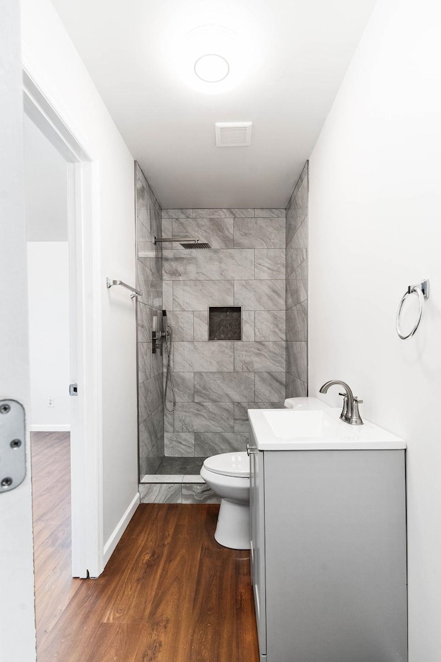 bathroom featuring tiled shower, hardwood / wood-style floors, vanity, and toilet