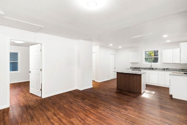 kitchen featuring white cabinetry, a center island, sink, light stone counters, and dark hardwood / wood-style flooring