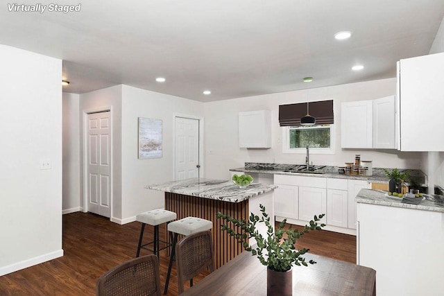 kitchen with white cabinetry, sink, light stone counters, dark hardwood / wood-style floors, and a kitchen island