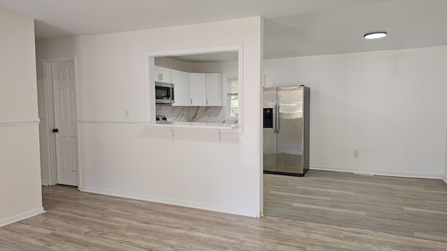 kitchen featuring tasteful backsplash, white cabinetry, stainless steel appliances, and light hardwood / wood-style flooring