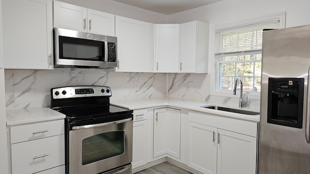 kitchen with backsplash, stainless steel appliances, white cabinetry, and sink