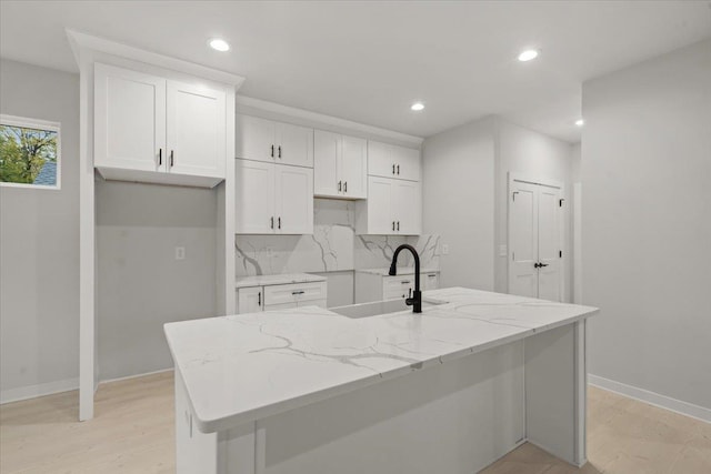 kitchen with a kitchen island with sink, sink, white cabinets, and light stone countertops