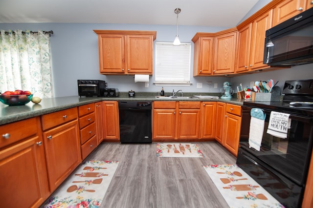 kitchen with decorative light fixtures, sink, light hardwood / wood-style floors, and black appliances