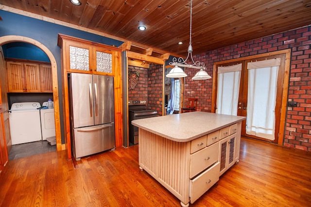 kitchen featuring washer and clothes dryer, a kitchen island, brick wall, and appliances with stainless steel finishes