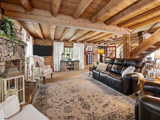 living room featuring a stone fireplace, beamed ceiling, and wood ceiling