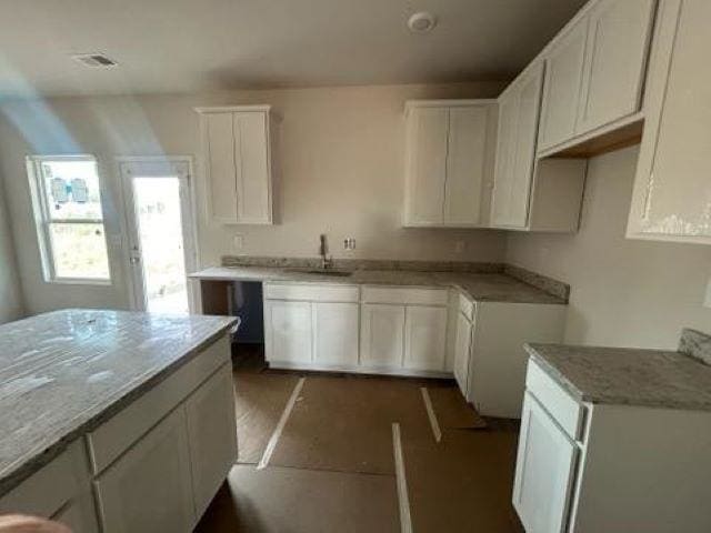 kitchen featuring light stone counters, white cabinetry, and sink