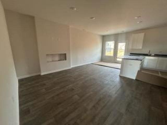 unfurnished living room featuring dark wood-type flooring and baseboards