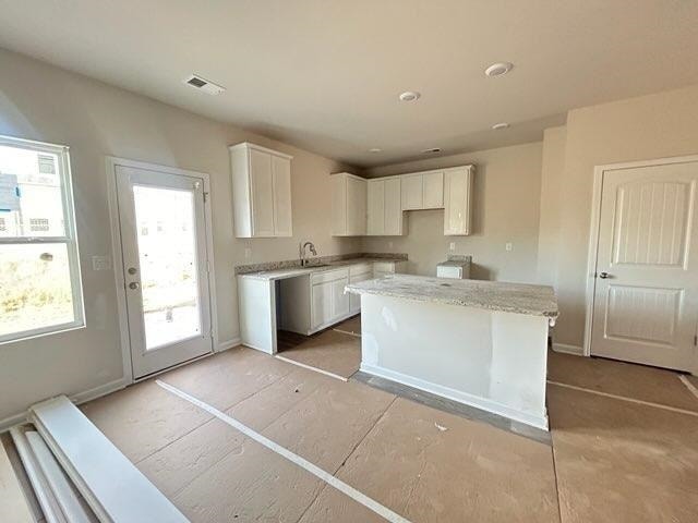 kitchen featuring baseboards, visible vents, light stone counters, a center island, and white cabinetry