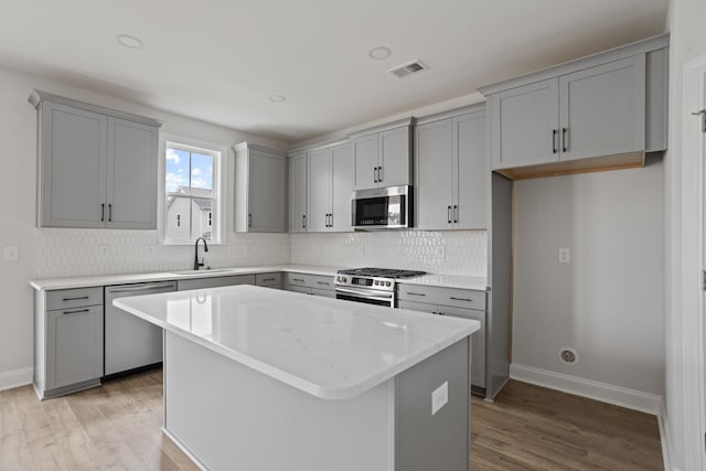 kitchen with sink, a center island, stainless steel appliances, light hardwood / wood-style flooring, and backsplash