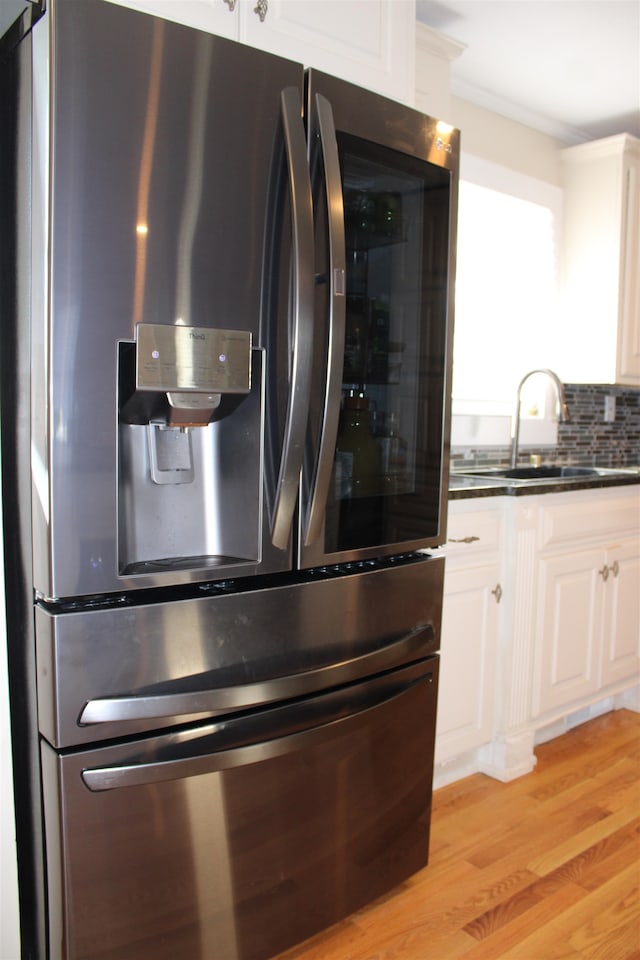 kitchen with backsplash, white cabinets, stainless steel fridge, light wood-type flooring, and ornamental molding