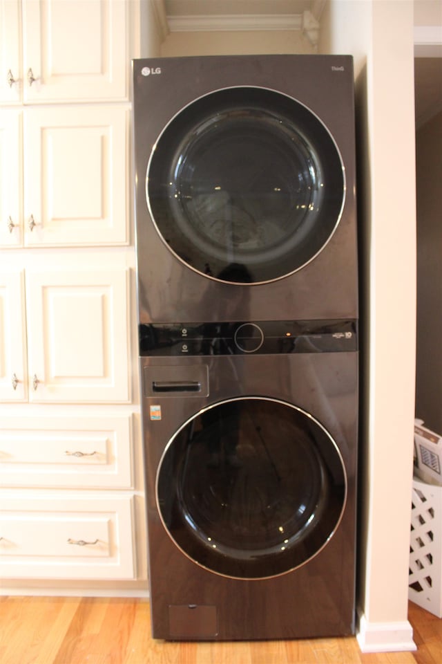 laundry area with cabinets, stacked washing maching and dryer, ornamental molding, and light wood-type flooring