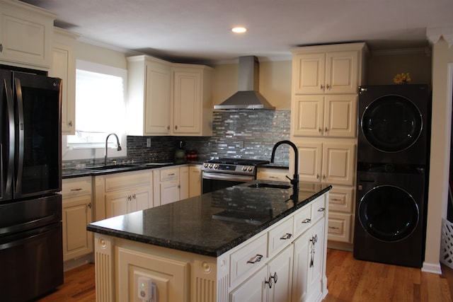 kitchen featuring black fridge, stacked washer and dryer, wall chimney exhaust hood, and sink