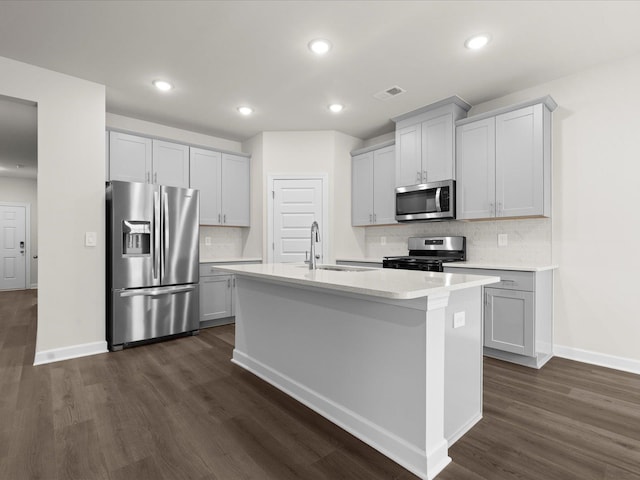 kitchen with sink, appliances with stainless steel finishes, dark hardwood / wood-style floors, an island with sink, and backsplash