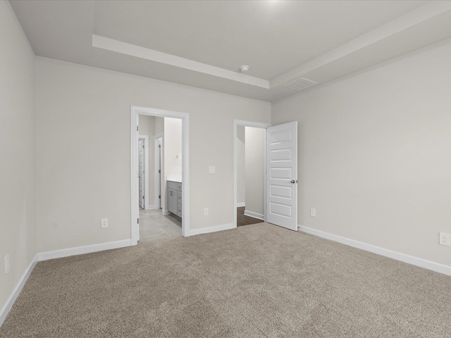 unfurnished bedroom with connected bathroom, a tray ceiling, and light carpet