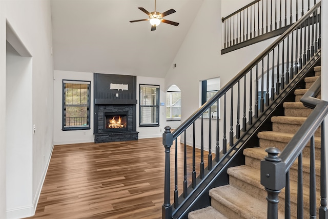 stairs featuring ceiling fan, wood-type flooring, a fireplace, and high vaulted ceiling