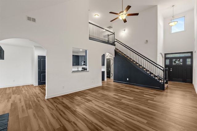 unfurnished living room with ceiling fan, wood-type flooring, and a high ceiling