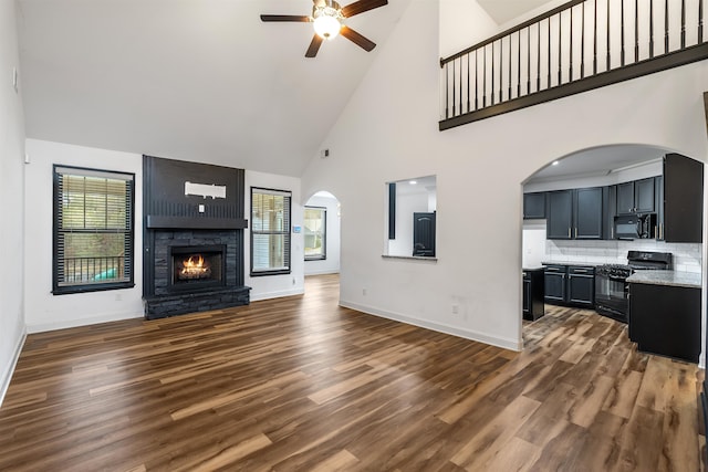 unfurnished living room featuring a large fireplace, dark hardwood / wood-style floors, ceiling fan, and high vaulted ceiling