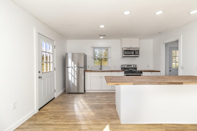 kitchen with appliances with stainless steel finishes, light wood-style flooring, wood counters, and a sink