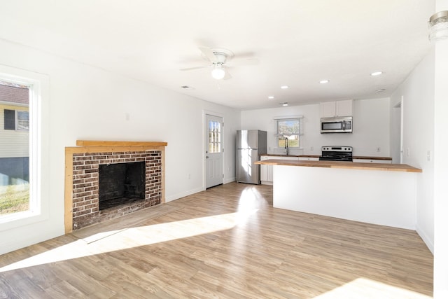 kitchen featuring light wood-style flooring, butcher block countertops, appliances with stainless steel finishes, a peninsula, and a brick fireplace