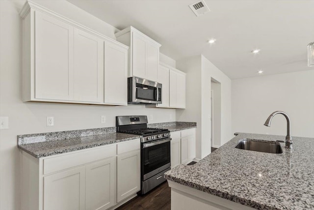 kitchen featuring sink, dark wood-type flooring, light stone counters, white cabinets, and appliances with stainless steel finishes