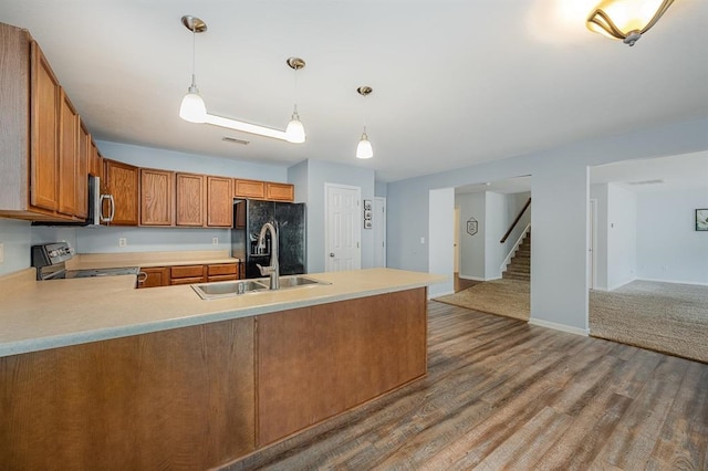 kitchen featuring sink, stainless steel appliances, kitchen peninsula, pendant lighting, and wood-type flooring