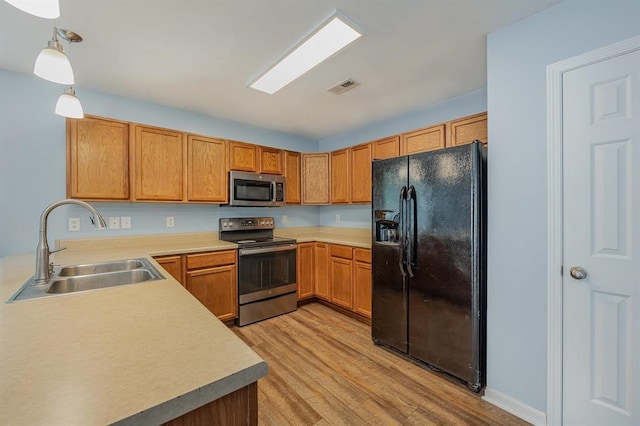 kitchen with appliances with stainless steel finishes, decorative light fixtures, light hardwood / wood-style flooring, and sink