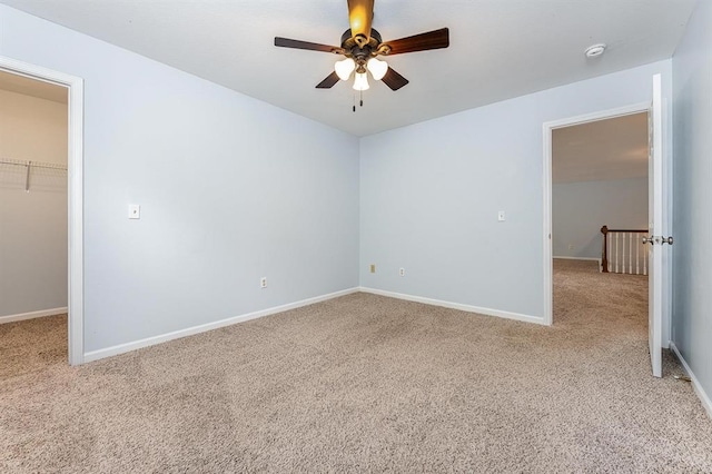 unfurnished bedroom with light carpet, a walk in closet, a closet, and ceiling fan