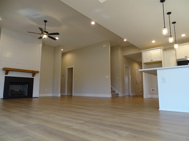 unfurnished living room with ceiling fan, light wood-type flooring, a fireplace, and a towering ceiling