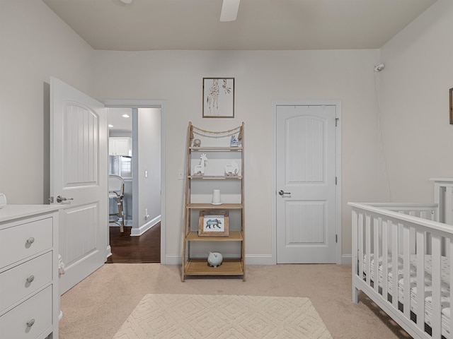 bedroom with ceiling fan, light colored carpet, and a nursery area