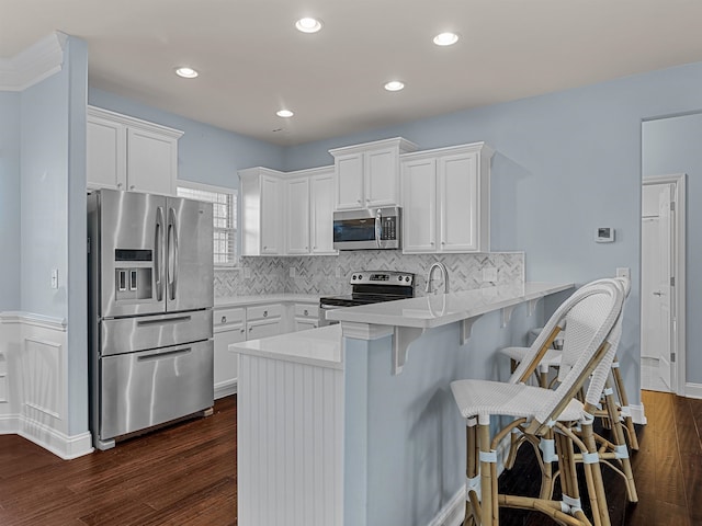 kitchen with stainless steel appliances, dark hardwood / wood-style floors, kitchen peninsula, a breakfast bar, and white cabinets