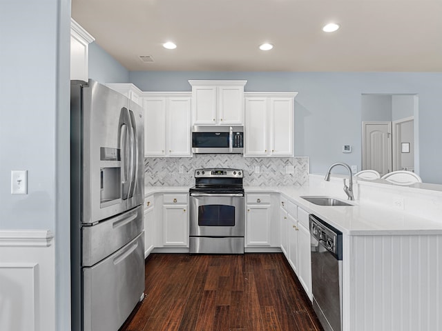 kitchen with dark wood-type flooring, sink, appliances with stainless steel finishes, white cabinetry, and kitchen peninsula