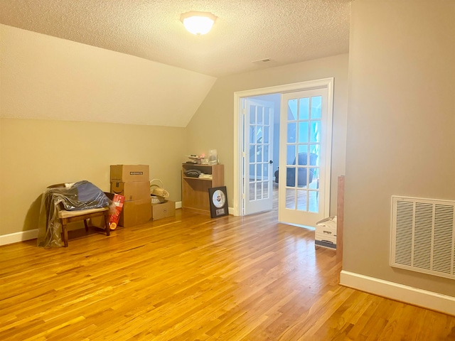 additional living space with light hardwood / wood-style floors, lofted ceiling, a textured ceiling, and french doors