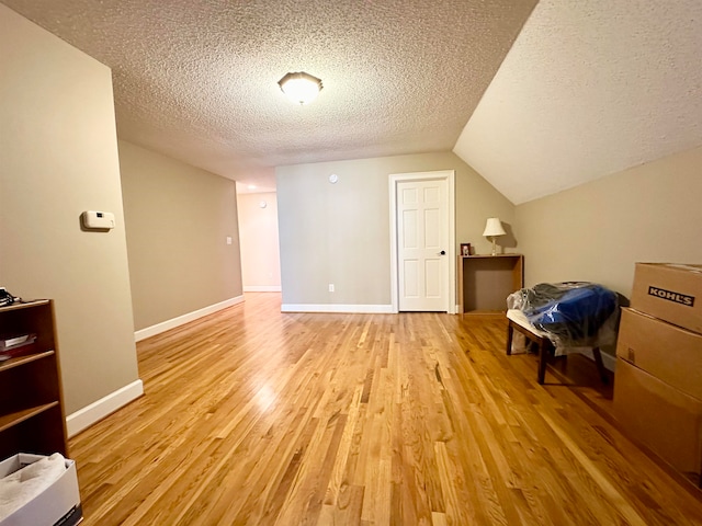 additional living space with a textured ceiling, light hardwood / wood-style flooring, and lofted ceiling