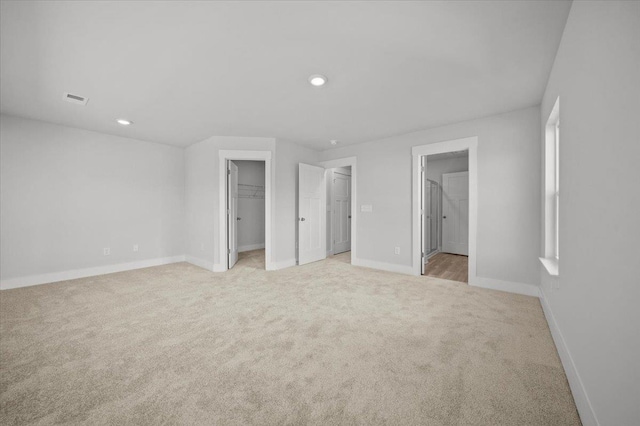 unfurnished bedroom featuring light colored carpet, connected bathroom, a closet, and a walk in closet