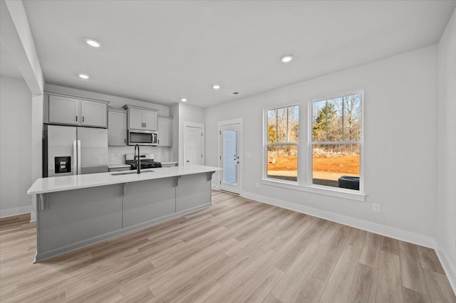 kitchen featuring gray cabinets, sink, stainless steel appliances, a center island with sink, and light hardwood / wood-style flooring