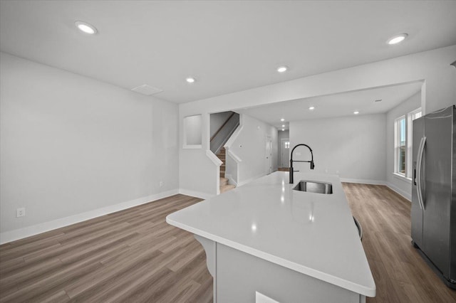 kitchen featuring wood-type flooring, sink, a kitchen island with sink, and stainless steel fridge with ice dispenser