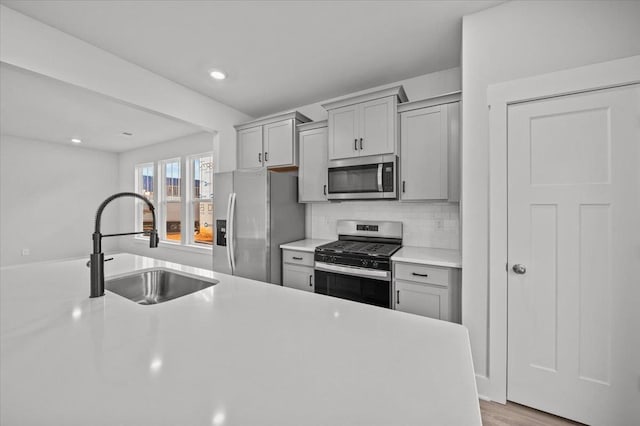 kitchen featuring gray cabinets, sink, backsplash, stainless steel appliances, and light hardwood / wood-style flooring