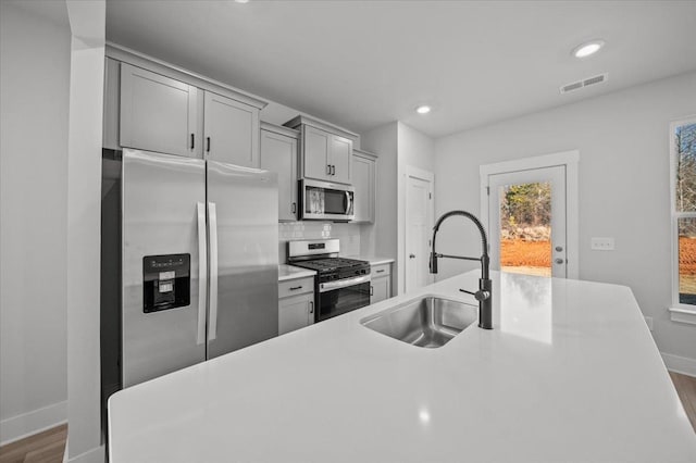 kitchen with gray cabinets, dark hardwood / wood-style floors, sink, decorative backsplash, and stainless steel appliances