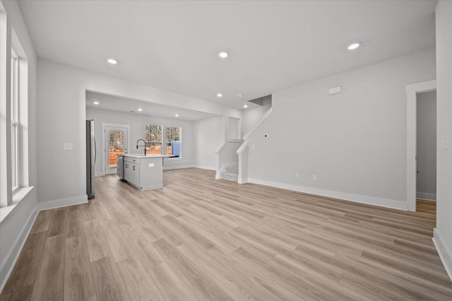 unfurnished living room featuring sink and light hardwood / wood-style floors