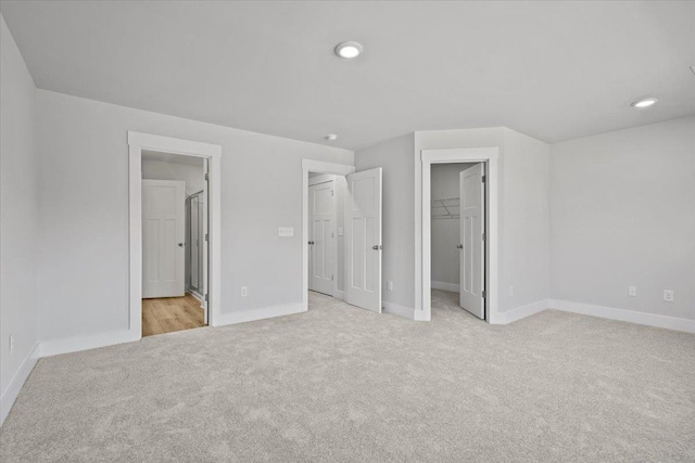 unfurnished bedroom featuring a walk in closet, ensuite bath, a closet, and light carpet