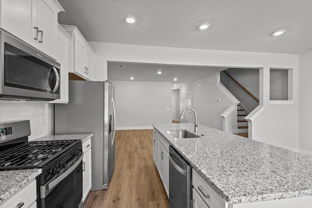 kitchen featuring appliances with stainless steel finishes, white cabinetry, sink, a kitchen island with sink, and light stone counters